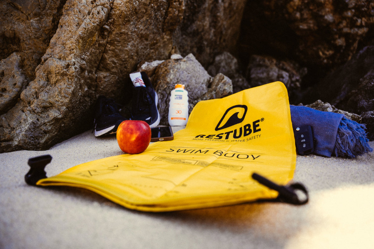 Se muestra la boya de senalizacion RESTUBE PRO desinflada y con la seccion de bolsa seca abierta para poder guardar diferentes cosas en su interior, como una crema de proteccion solar, una manzana, o llaves del auto. Para que lleves todo contigo durante el entrenamiento en el agua