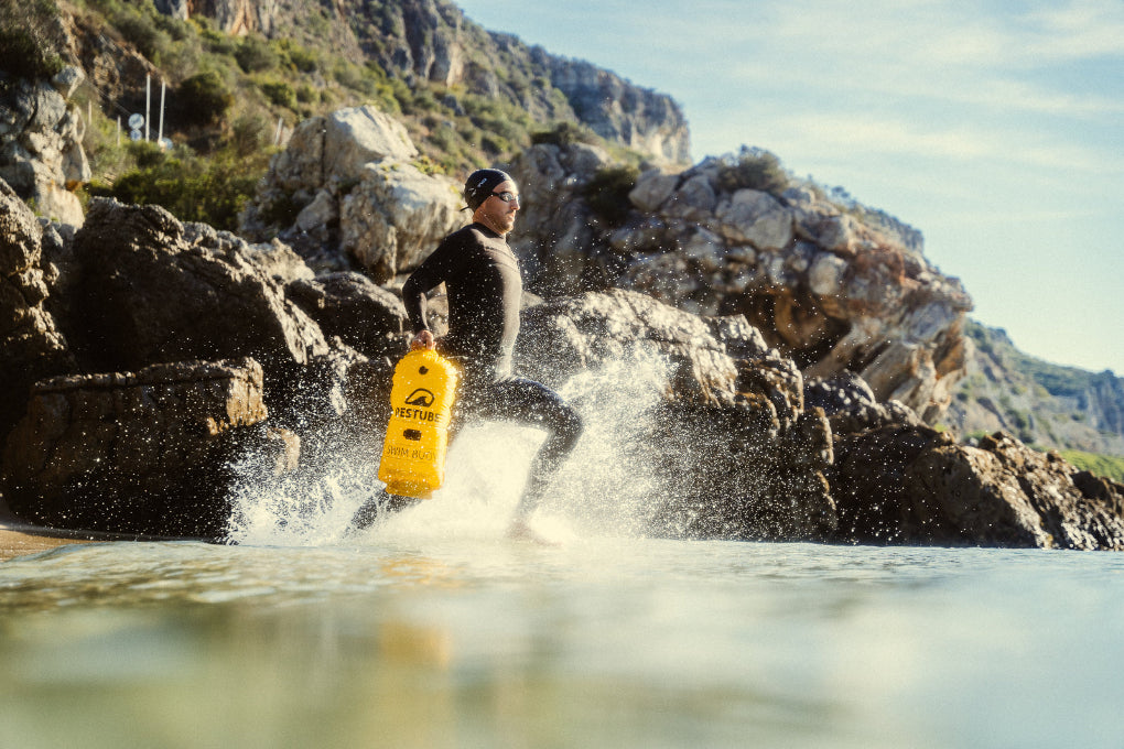 Esta foto muestra a un nadador de aguas abiertas corriendo con una boya de sanalizacion RESTUBE PRO entrando al mar. Listo para ingresar al agua y contar con flotacion extra y mucha más seguridad durante el entrenamiento
