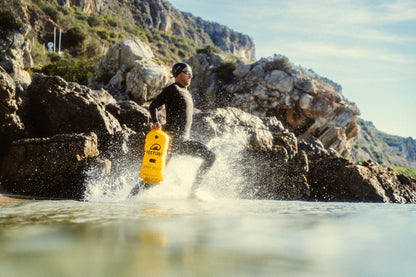 Esta foto muestra a un nadador de aguas abiertas corriendo con una boya de sanalizacion RESTUBE PRO entrando al mar. Listo para ingresar al agua y contar con flotacion extra y mucha más seguridad durante el entrenamiento